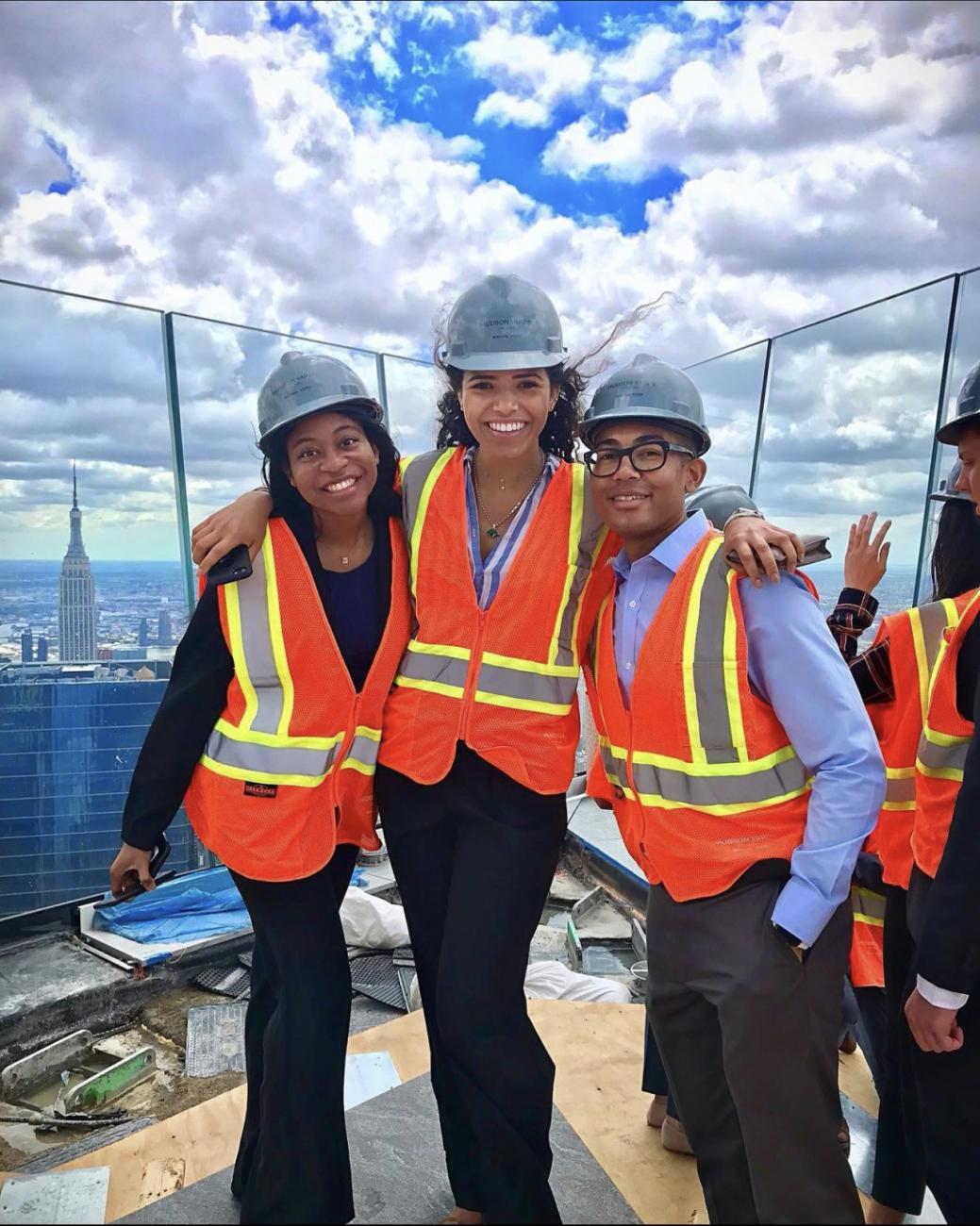 Three Davis Polk summer associates wearing hard hats on the top of a skyscraper